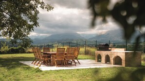 An outdoor dining area with a table and chairs, a brick barbecue grill, and a view of mountains. - Cosy apartment on a tranquil estate with shared pool & mountain views (Marche)