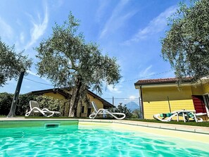 A swimming pool with lounge chairs, a yellow building, and trees. - Apartment Blue by Interhome (Albisano)