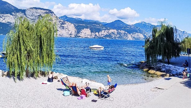 Una spiaggia con persone che si rilassano, una barca nell'acqua e montagne sullo sfondo.