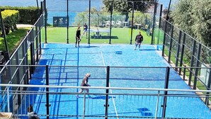 Un campo da tennis all'aperto con una rete, circondato da una recinzione metallica.