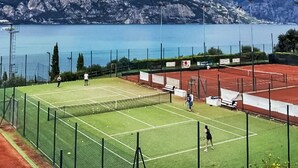 Un campo da tennis con una rete, circondato da una recinzione, con montagne e un lago sullo sfondo.