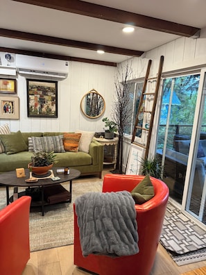 A cozy living room with a green sofa, red chairs, a coffee table, and a large window with a view of trees.