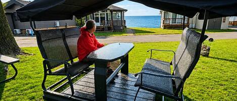 A covered outdoor seating area with a table and chairs, overlooking a body of water and residential buildings.