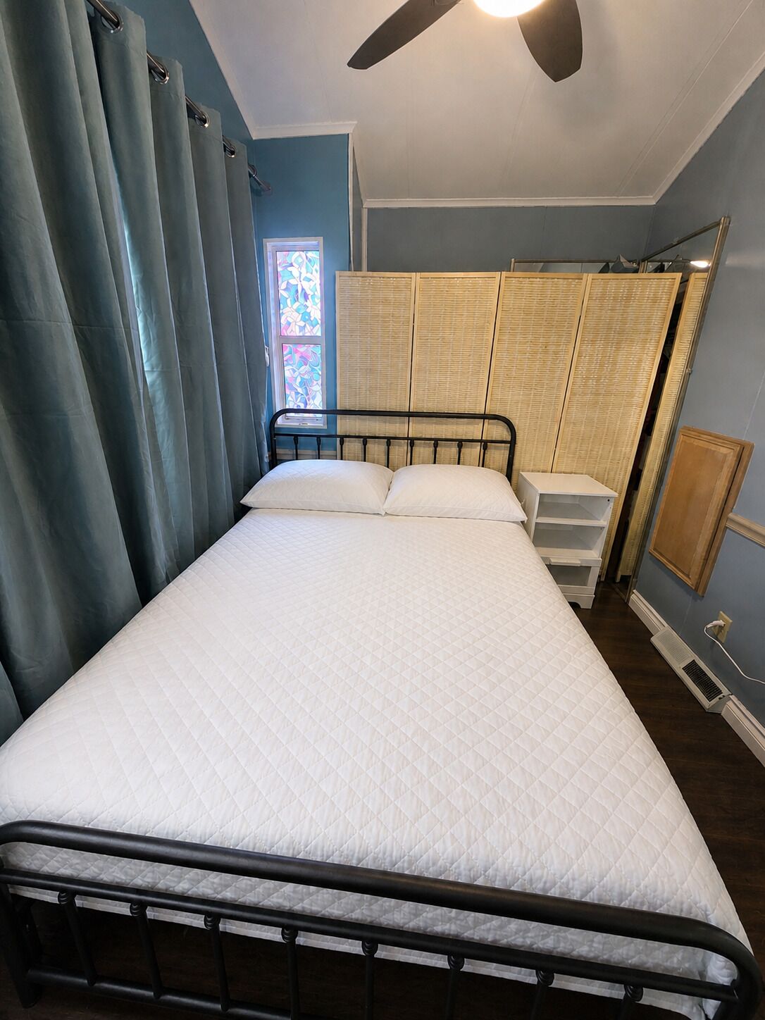 A bedroom with a bed, a ceiling fan, a window with stained glass, and a wardrobe.