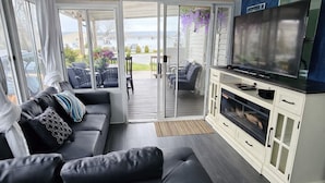 A modern interior with a black leather sofa, a flat-screen TV, and a sliding glass door leading to an outdoor patio. - Sun Retreats Sherkston Shores (Port Colborne)