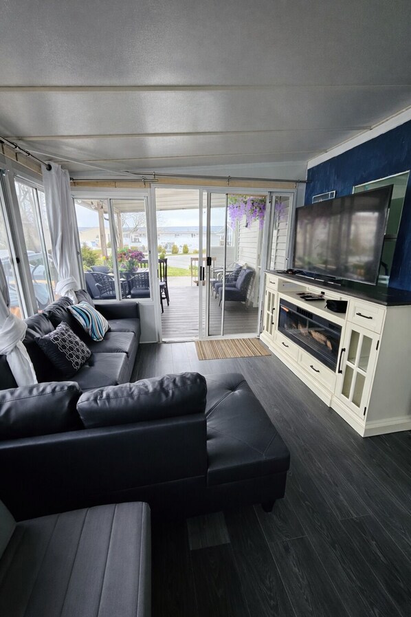 A modern interior with a black leather sofa, a flat-screen TV, and a sliding glass door leading to an outdoor patio. - Sun Retreats Sherkston Shores (Port Colborne)