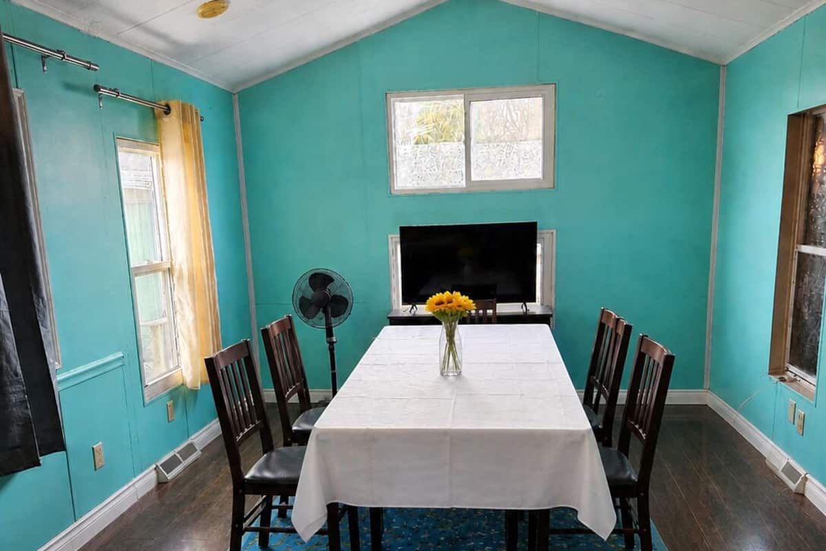 A dining room with a white table, chairs, a fan, and a TV.