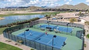 Complejo de canchas de tenis con varias pistas, rodeado por una cerca y un cuerpo de agua al fondo.