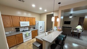 Cocina con gabinetes de madera, microondas, estufa, refrigerador y una barra con taburetes.