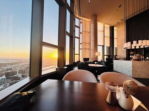 A modern hotel room with a large window offering a city view, a dining area with a table and chairs, and a bar area with a marble countertop. - Royal Executive Living  Sky Corporate Residence (Melbourne)