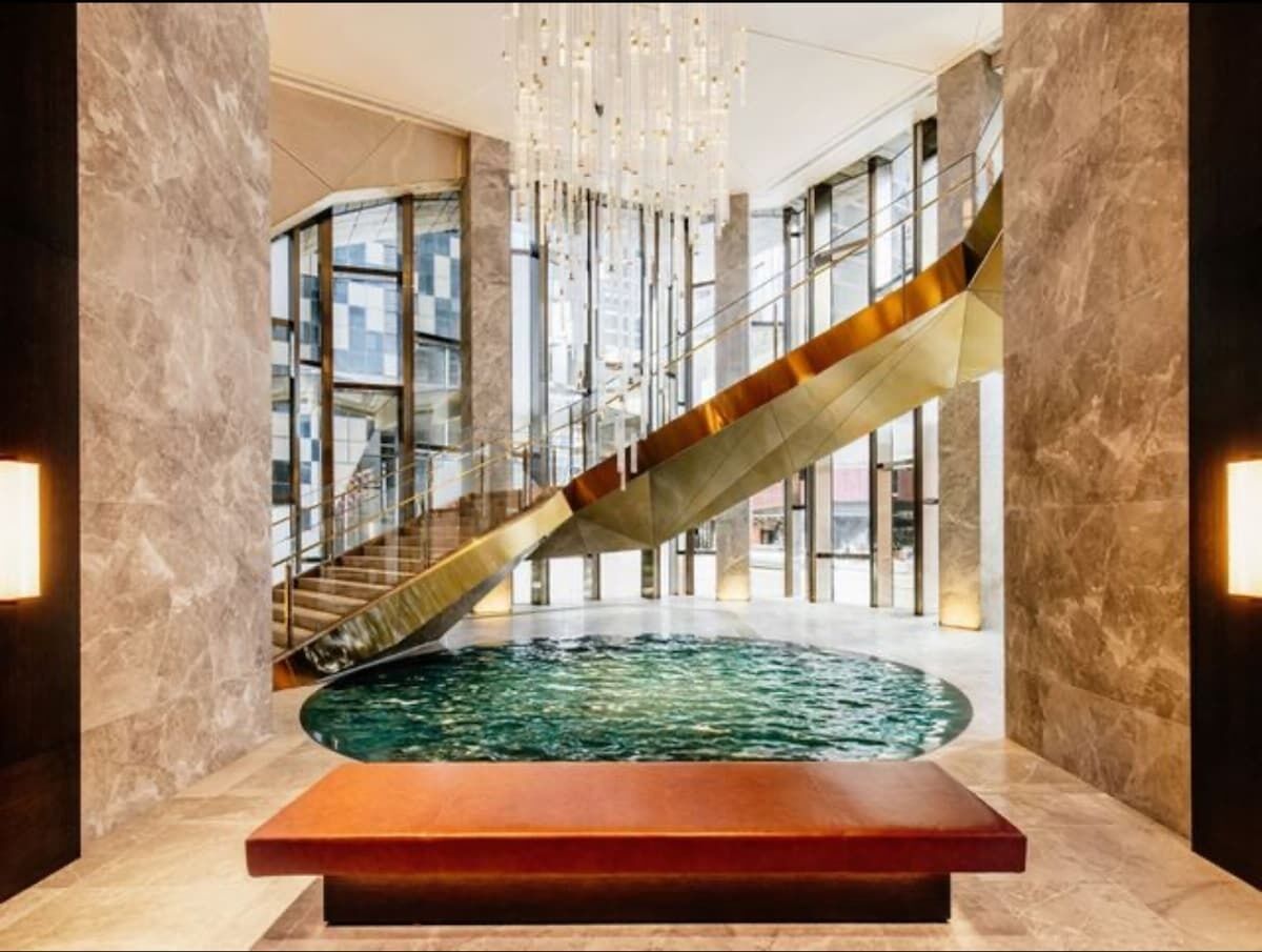 Ein modernes Interieur mit einem zentralen Wasserspiel, einer Glaskonstruktion als Treppe und einem Chandelier.