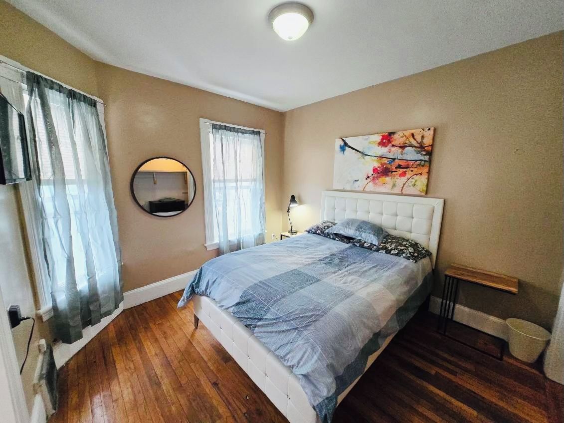 A bedroom with a bed, a round mirror, a painting, and a bedside table.