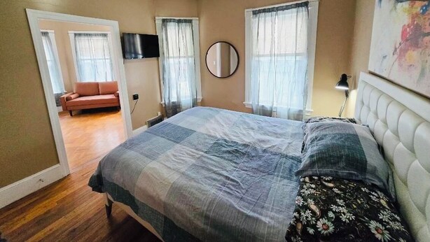 A bedroom with a bed, a television, a mirror, and a painting on the wall.