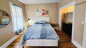 A bedroom with a bed, a bedside table, a lamp, a mirror, and a window with curtains.