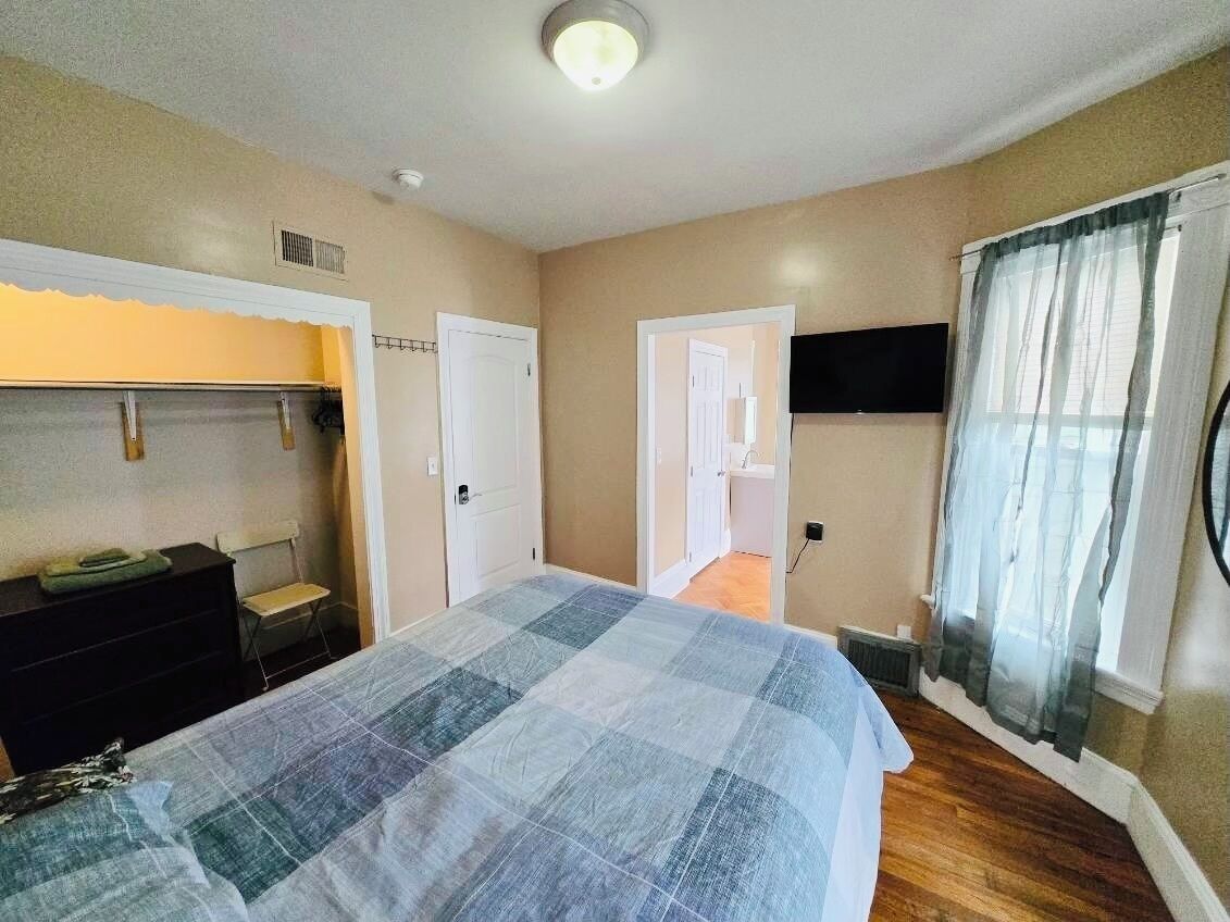 A bedroom with a bed, dresser, and a television mounted on the wall.