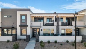 A modern two-story house with a covered patio, a stone facade, and a gravel driveway. - Sun-Filled Coastal Home | Lagoon Access| Hot Tub| Sleeps 12 (St. George)