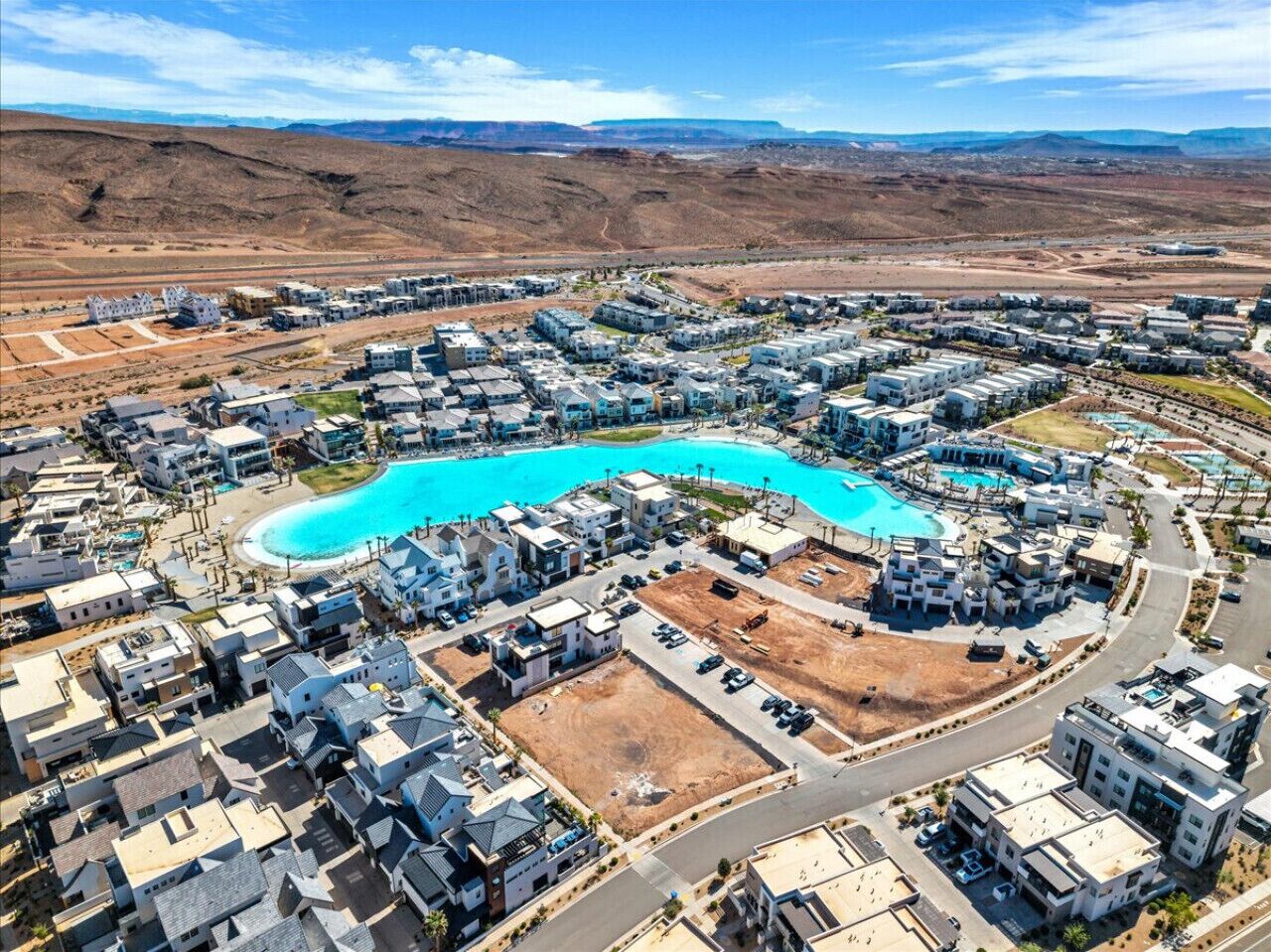 An aerial view of a residential area with modern houses, a large swimming pool, and a desert landscape in the background.