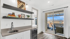 A modern kitchen with a sink, shelves, and a view of a desert landscape through a sliding glass door. - Sun-Filled Coastal Home | Lagoon Access| Hot Tub| Sleeps 12 (St. George)
