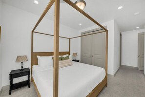 Una cama con dosel sobre un marco de madera, una mesita de noche con lámpara, un armario y una puerta en un dormitorio.