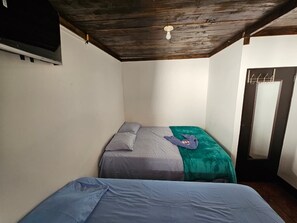 Quarto pequeno com duas camas, teto de madeira e porta com espelho.