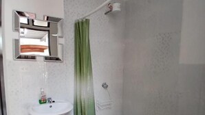 A bathroom with a pedestal sink, a toilet, a shower with a green curtain, and a mirror with a towel rack. - Hotel y restaurante pura vida (Antigua Guatemala)
