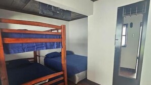 A room with a bunk bed, a single bed, a tiled floor, and a door with a mirror. - Hotel y restaurante pura vida (Antigua Guatemala)