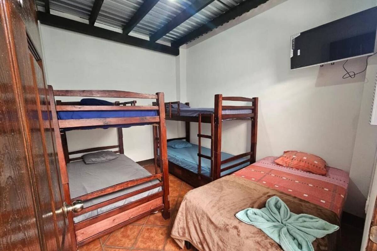 Ein Zimmer mit drei Etagenbetten, einem Einzelbett, einer Holztür und einem Fliesenboden.