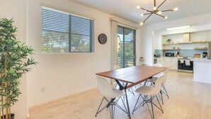 Une cuisine moderne avec des armoires blanches, un four encastré et un coin repas comprenant une table en bois et quatre chaises.