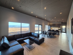 Ein modernes Wohnzimmer mit einem Ecksofa, einem Glastisch und großen Fenstern mit Blick auf eine Wüstenlandschaft.