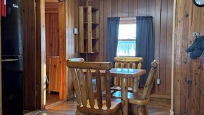 A wooden interior with a dining table and chairs, a refrigerator, and a clock on the wall. - Beavers Resort - Cabin 1 (Mercer)