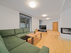 Een moderne woonkamer met een groene bank, een houten salontafel, een televisie en een open haard.