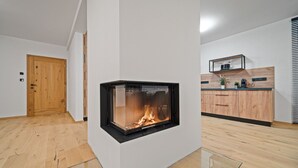 Un salon moderne doté d’une cheminée, de planchers en bois, d’un coin cuisine avec des armoires en bois et d’une porte.