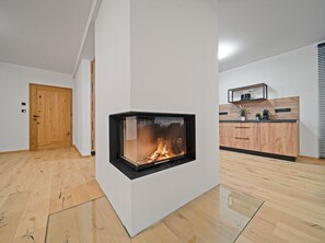Una sala de estar moderna con chimenea, suelo de madera, una zona de cocina con armarios de madera y una puerta.