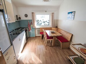 A compact kitchen with a stove, sink, and wooden dining table with benches. - Apartment Veglia by Interhome (Samedan)