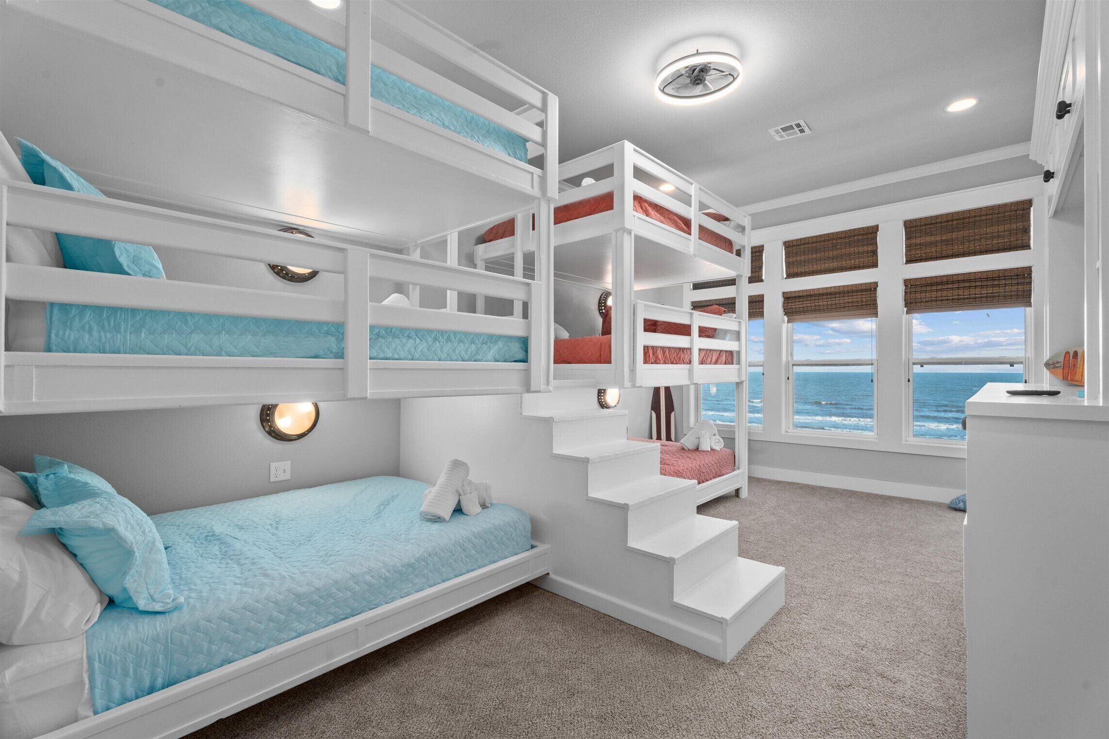 Ein Mehrbettzimmer mit Stockbetten und Meerblick, inklusive Treppe und Deckenventilator.