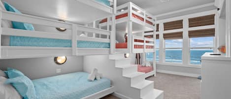Ein Mehrbettzimmer mit Stockbetten und Meerblick, inklusive Treppe und Deckenventilator.