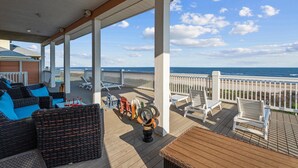 A covered outdoor deck with wicker furniture, white chairs, and a view of the ocean. - Beachfront Retreat Sleeps 30 with Swim Spa, Fire Pit and Putt-Putt (Bolivar Peninsula)