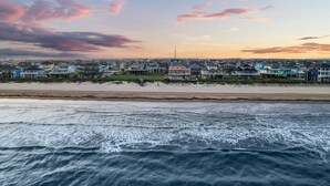 A coastal residential area with houses along the beachfront, a pier, and a tower in the distance. - Beachfront Retreat Sleeps 30 with Swim Spa, Fire Pit and Putt-Putt (Bolivar Peninsula)