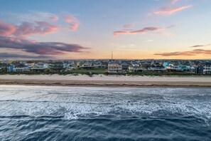 A coastal residential area with houses along the beachfront, a pier, and a tower in the distance. - Beachfront Retreat Sleeps 30 with Swim Spa, Fire Pit and Putt-Putt (Bolivar Peninsula)
