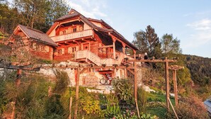 Ein traditionelles Holzhäuschen mit Balkon, umgeben von üppigem Grün und einer Bergkulisse.