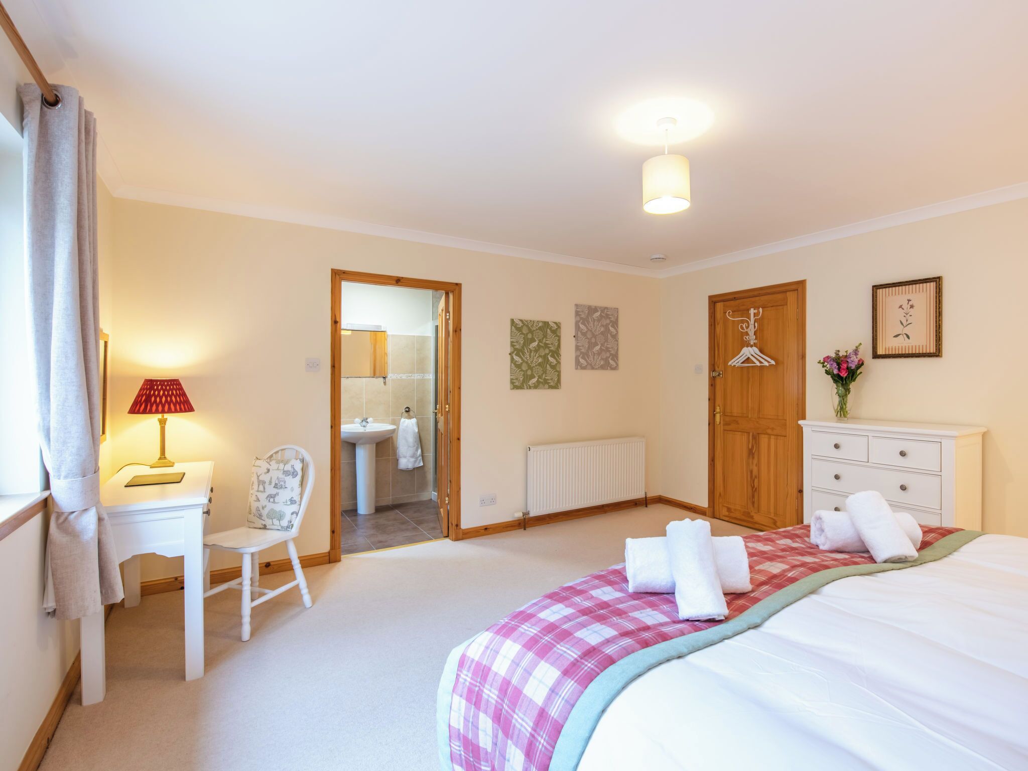 A bedroom with a bed, a desk, a chair, a radiator, a wooden door, and a bathroom visible through an open door.