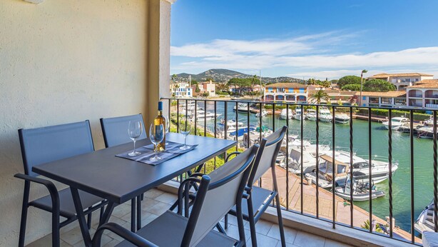 Ein Balkon mit Tisch für zwei Personen, mit Blick auf eine Marina mit Booten und Gebäuden.