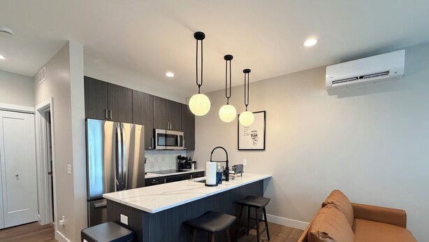Una cocina moderna con una isla central, taburetes de bar e iluminación colgante.