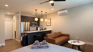 Una habitación de hotel moderna con una cama grande, un sofá, una pequeña cocina y un ventilador de techo.