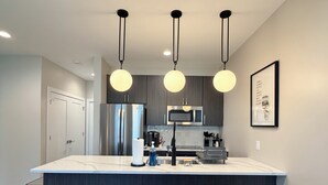 Una cocina moderna con una isla central, electrodomésticos de acero inoxidable, iluminación colgante y una obra de arte enmarcada en la pared.
