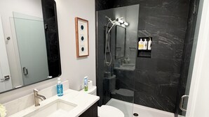 Un baño moderno con tocador de doble lavamanos, inodoro, ducha envuelta en vidrio y salpicadero de mármol.
