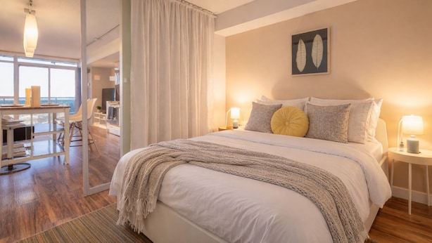 A modern bedroom with a large bed, bedside lamps, and a view of the city. - 2 Bedroom Luxury Apartment in Downtown Toronto (Toronto)