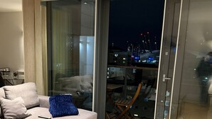 Ein modernes Wohnzimmer mit einem Ecksofa, einem Glastisch und Blick auf eine nächtliche Skyline.