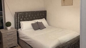 Ein Schlafzimmer mit Bett, Nachttisch, Lampe und einem an der Wand hängenden Kunstwerk.