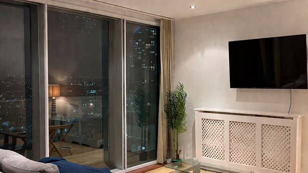 Ein modernes Wohnzimmer mit einer Couch, einem Glastisch, einem Fernseher und einer Schiebetür zu einem Balkon.